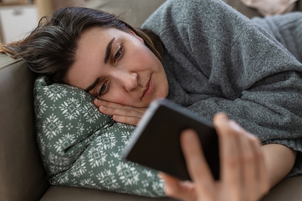 een vrouw ligt op de bank te doemscrollen op haar telefoon.