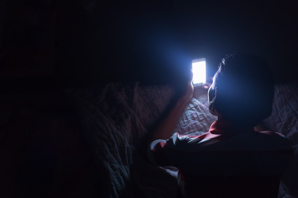 Een jong persoon kijkt in het donker naar een fel verlichte smartphone.