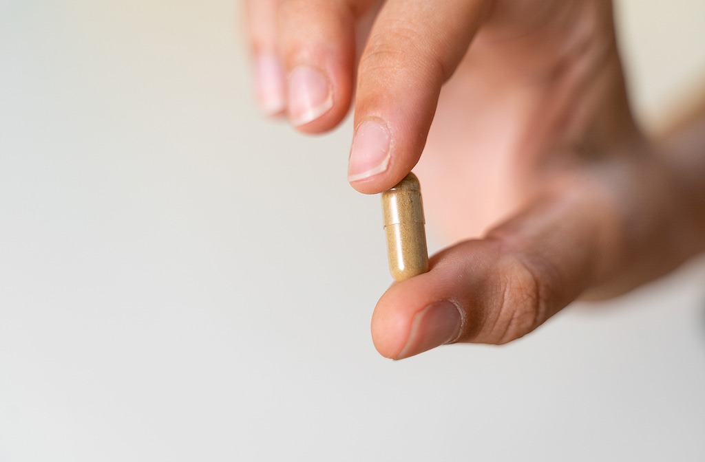 Iemand laat een capsule zien tussen 2 vingers.